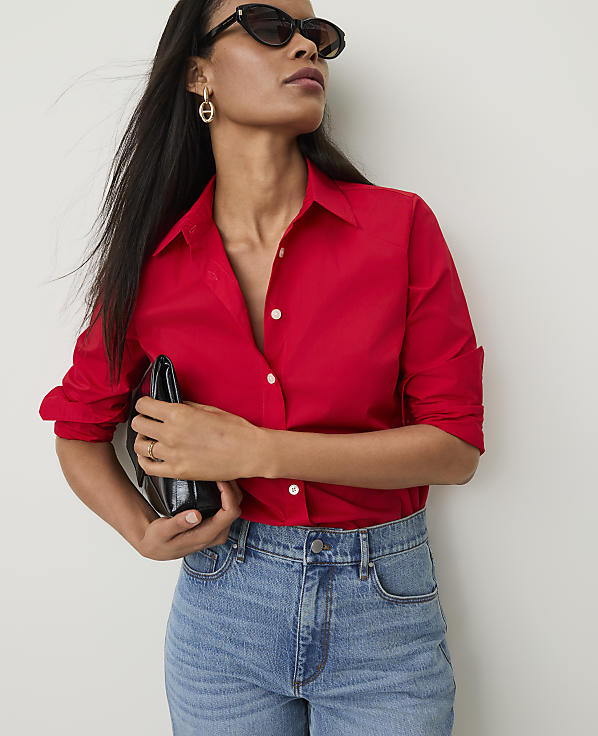 A woman in a red shirt and jeans holds a black clutch against a plain white background.