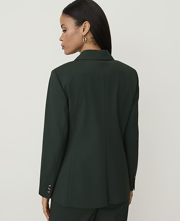 A woman in a dark green blazer stands against a plain white background.