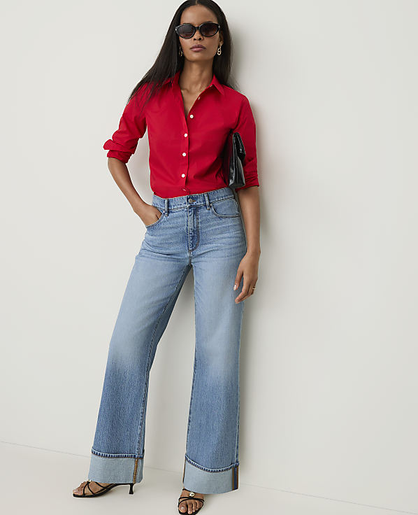 A woman in a red shirt and wide-leg jeans stands against a plain white background.