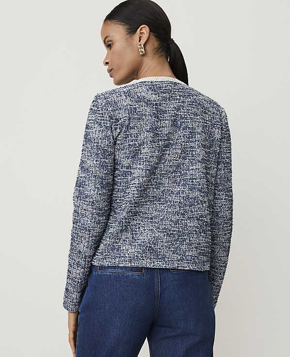 A woman in a textured blue jacket and dark jeans stands against a plain, light background.