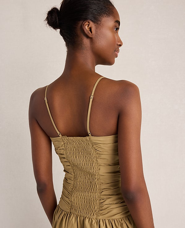 A woman in a smocked, olive-green dress is shown from the back against a plain, light-colored background.