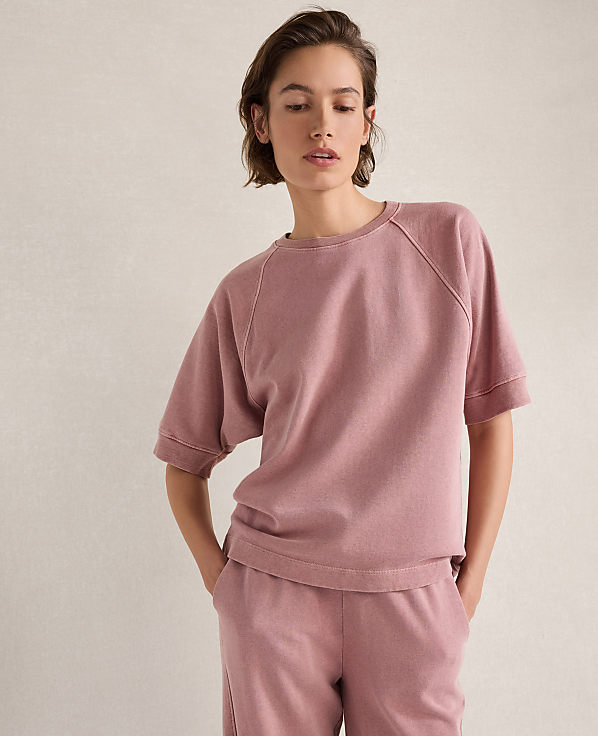 A woman in a pink sweatshirt and pants stands against a textured, light-colored background.