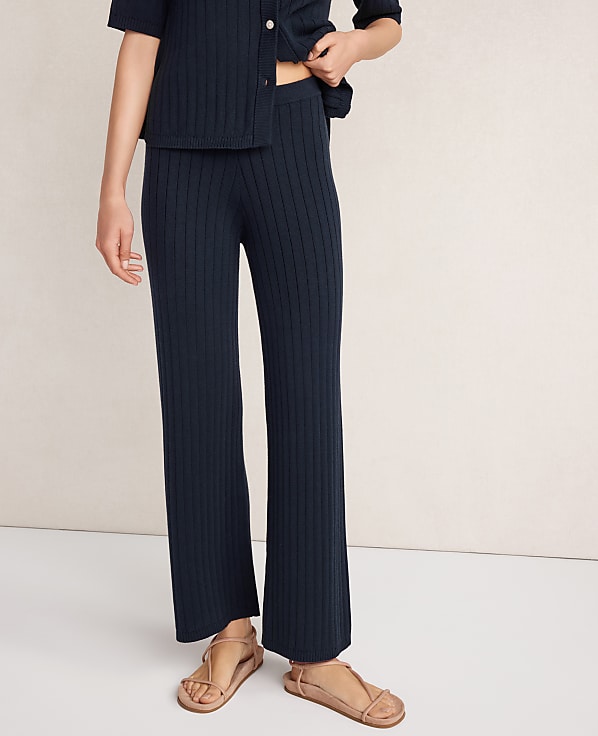 A person wearing navy ribbed knit pants and sandals stands against a plain, light-colored background.
