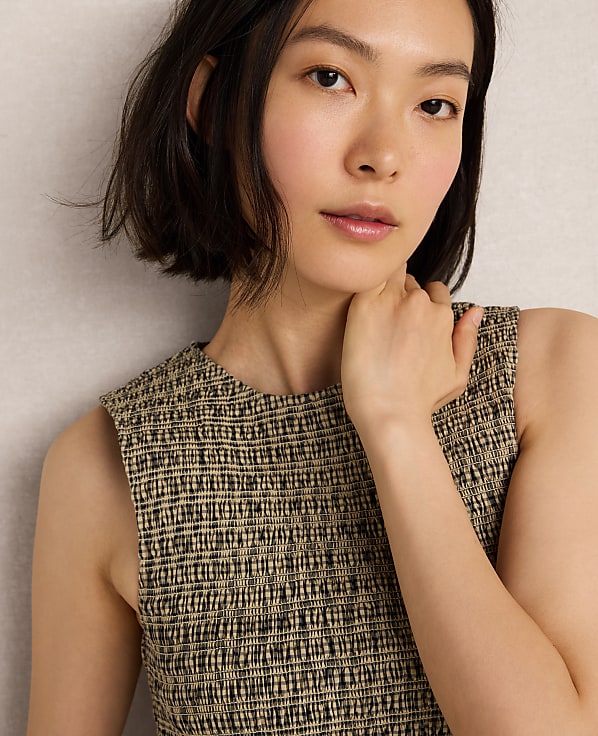A young woman with short dark hair and a textured sleeveless top is posed against a neutral, textured background.