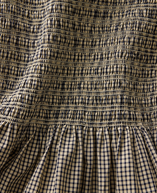 A close-up view of smocked fabric in the foreground transitions to a gathered gingham pattern in the background.