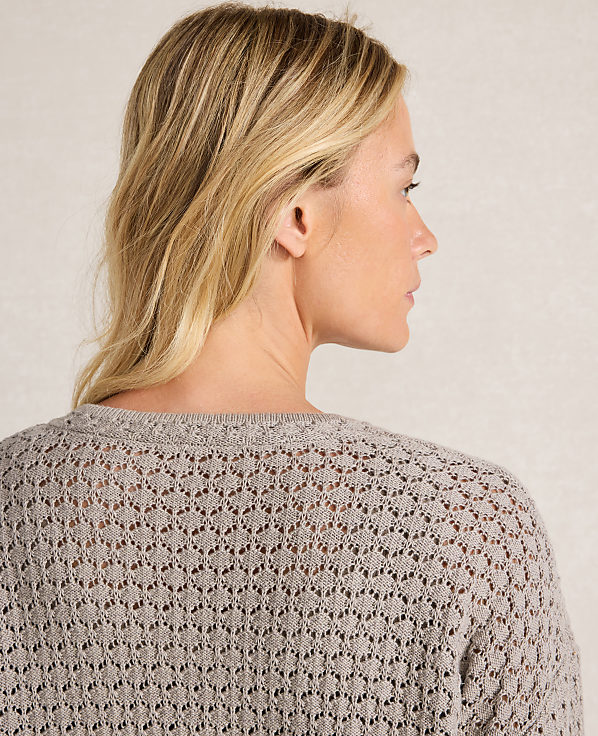 A woman with blonde hair is shown from the back, wearing a light gray, open-knit sweater against a neutral background.