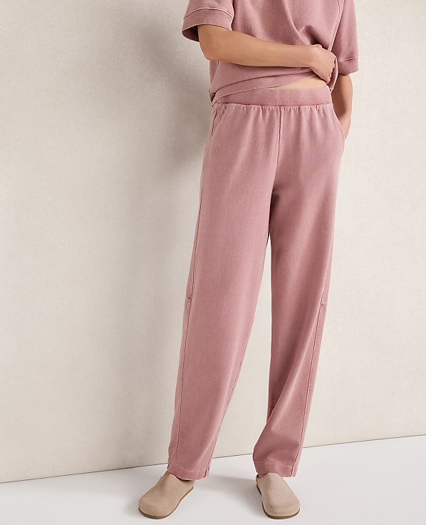 A person stands in loose-fitting pink loungewear with a plain, light-colored wall behind them.