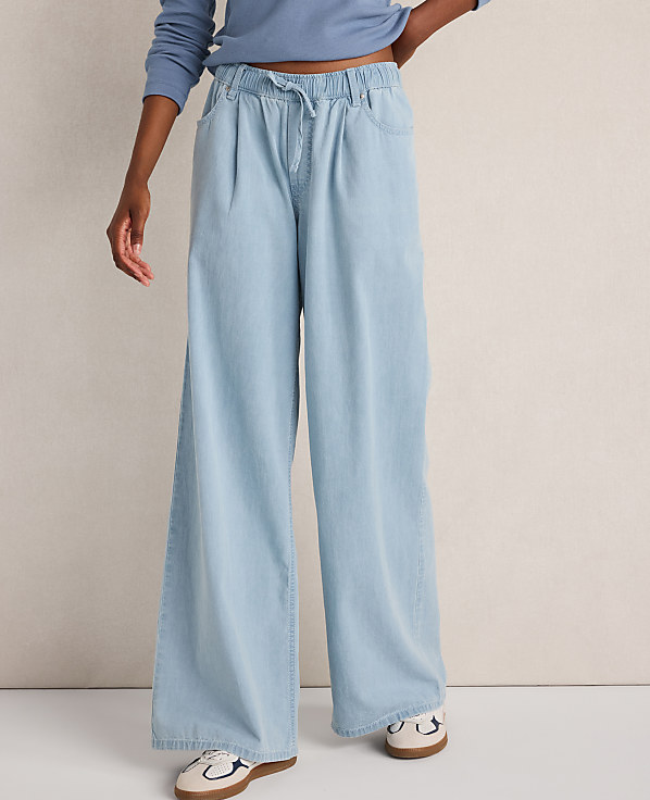 A person stands in light blue wide-leg jeans and sneakers against a plain white background.
