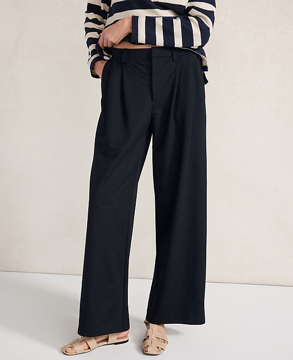 A person in dark, wide-leg pants and a striped shirt stands against a plain, light-colored background.