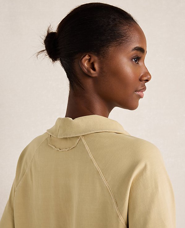 A woman with her hair in a bun wears a light yellow collared shirt against a plain, light background.