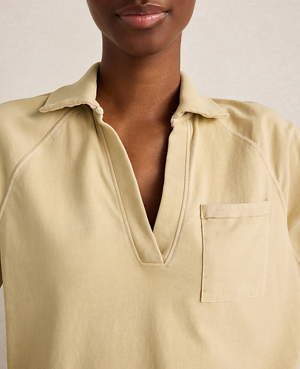 A close-up of a woman wearing a light yellow collared shirt with a pocket, against a plain, light background.