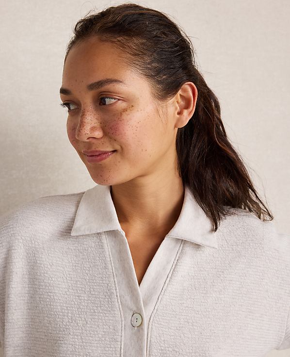 A woman with freckles and dark hair pulled back smiles gently in the foreground, against a softly textured, neutral background.