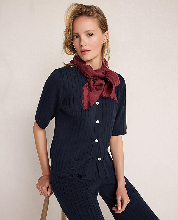 A woman in a navy ribbed outfit and a burgundy scarf sits against a plain, light background.