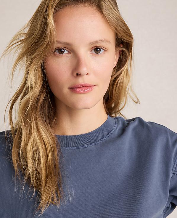 A young woman with blonde hair and a blue shirt is in the foreground, with a plain, light-colored background.