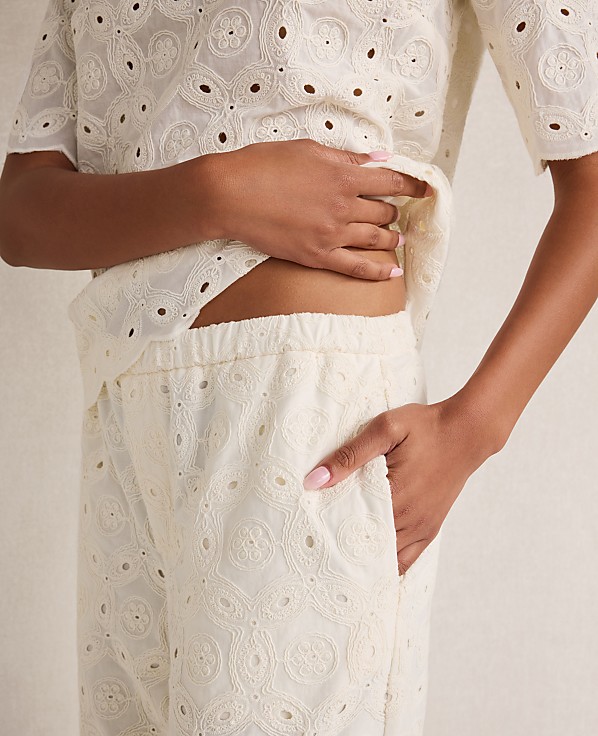 A person's torso, clad in cream-colored eyelet fabric, is framed against a plain, light-colored background.