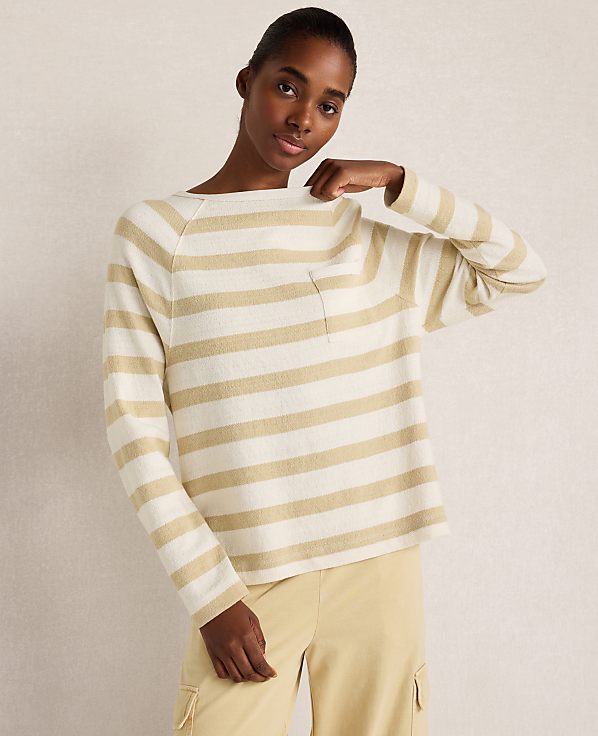A woman in a striped sweater and yellow pants stands against a plain background.