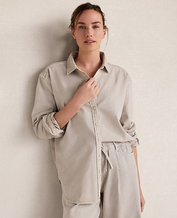A woman in a light-colored button-down shirt and pants stands against a textured, neutral wall.