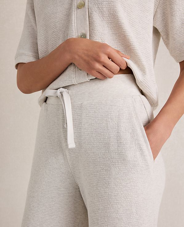 A person's hands are in the pockets of light-colored textured pajama pants, with a matching short-sleeved top visible above.
