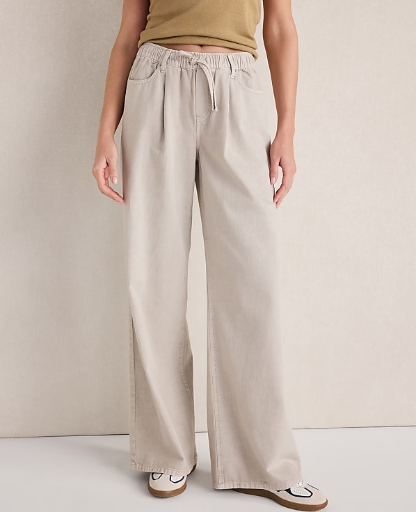 A person stands in loose-fitting beige pants and white shoes against a plain, light-colored background.