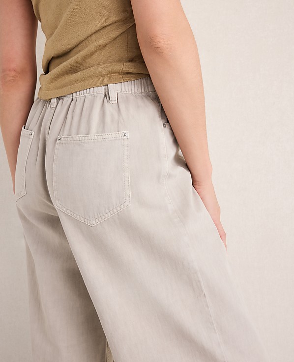 A person in light-colored pants and a tan top stands against a textured, light-colored wall.