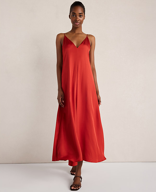 A woman in a flowing red slip dress stands against a plain, light-colored background.
