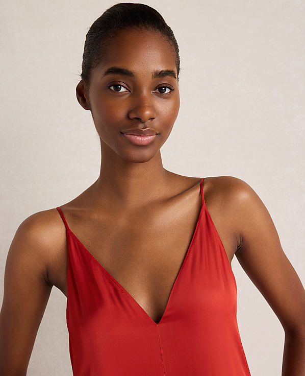 A young Black woman with dark hair pulled back wears a red V-neck dress against a plain, light-colored background.