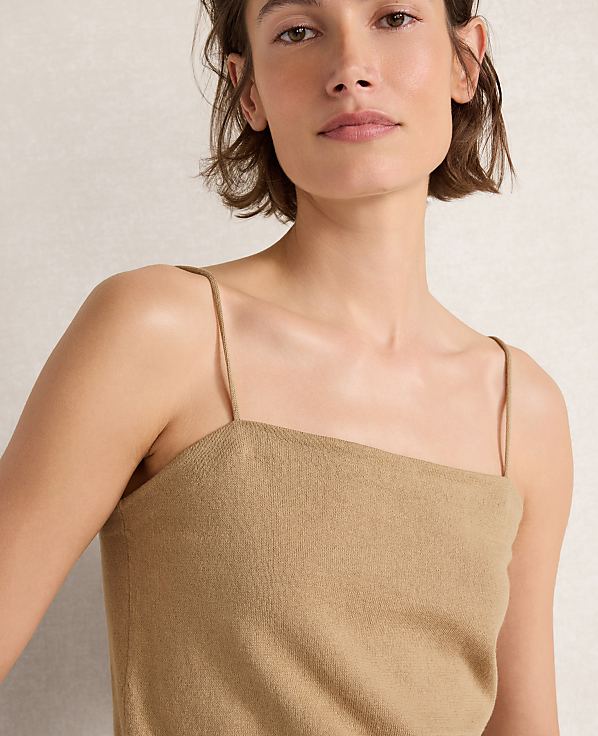 A woman with short brown hair wears a tan camisole in the foreground, against a softly lit, neutral background.