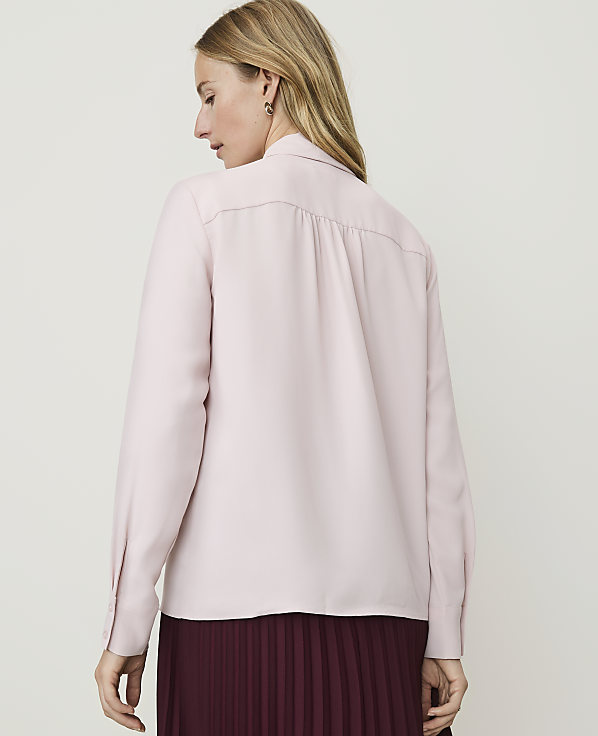 A woman in a pink blouse and burgundy pleated skirt stands against a plain white background.