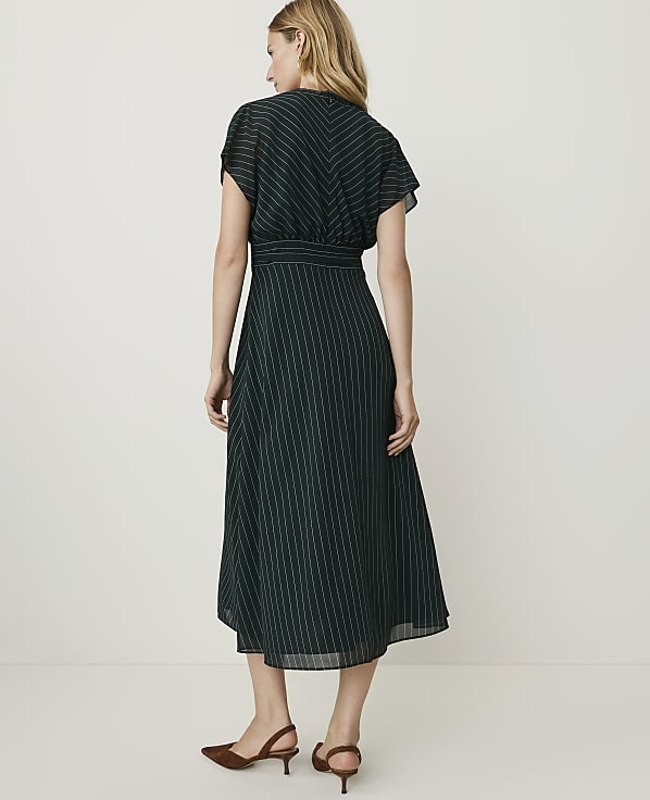 A woman in a dark green pinstripe dress stands against a plain, light-colored background.