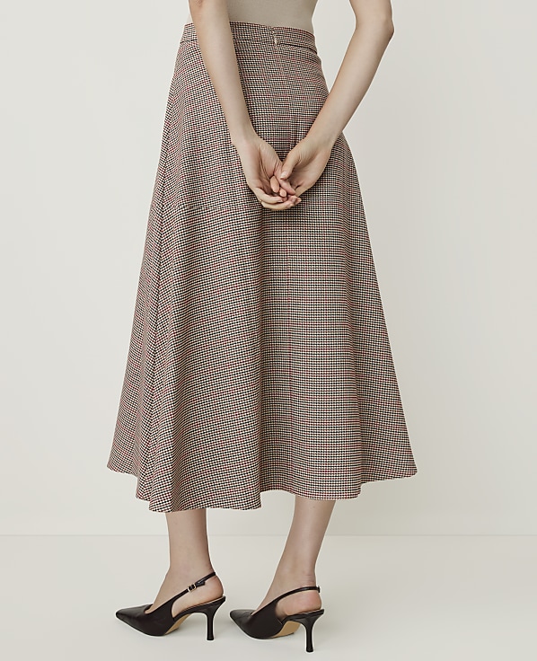 A woman in a plaid midi skirt and slingback heels stands against a plain white background.