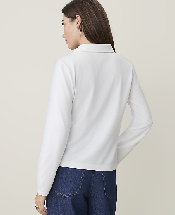 A woman in a white polo shirt and blue jeans stands against a plain, light-colored background.