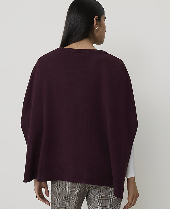 A woman wearing a burgundy poncho over a white shirt and plaid pants stands against a plain white background.