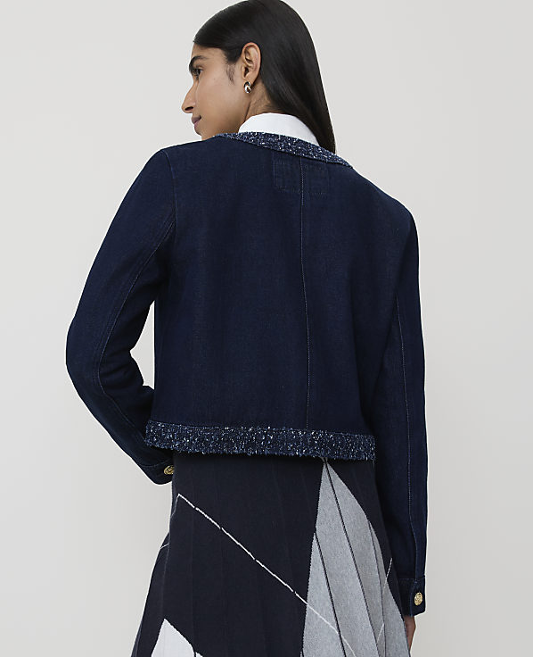 A woman in a denim jacket with a tweed trim stands against a plain white background.