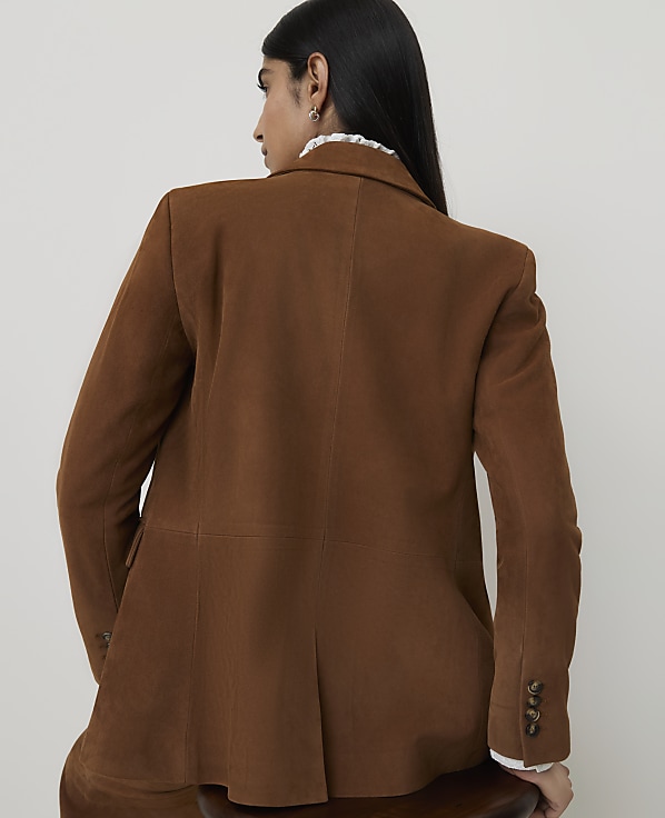 A woman in a brown corduroy blazer is shown from the back against a plain, light-colored background.