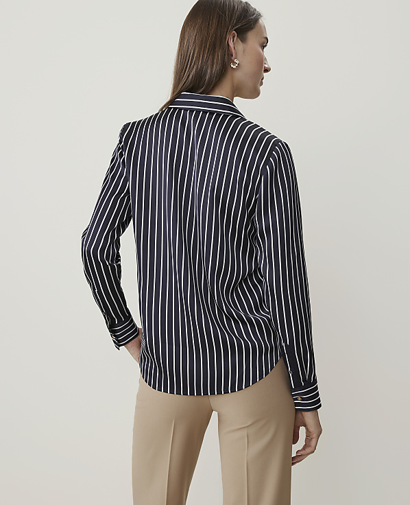 A woman in a black and white striped blouse and tan pants stands against a plain, light background.