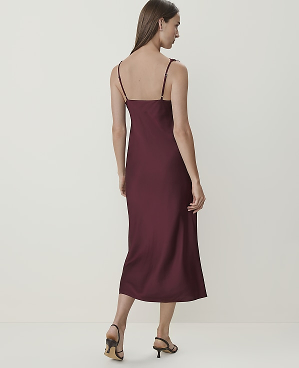 A woman in a burgundy slip dress stands against a plain, light-colored background.