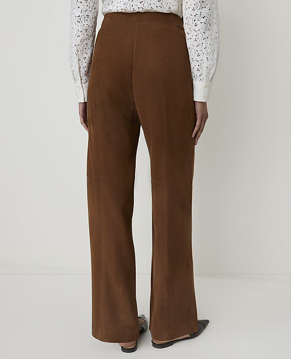 A person wearing brown corduroy pants and a white lace-trimmed shirt stands against a plain white background.