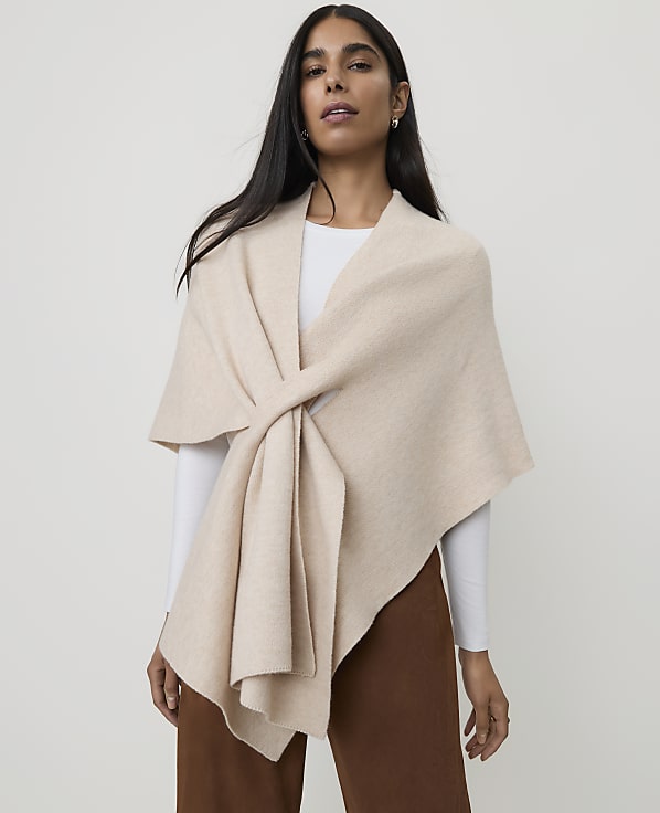 A woman in a cream-colored wrap stands against a plain, light background.