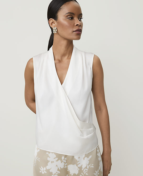 A woman in a white wrap top and floral skirt stands against a plain background.