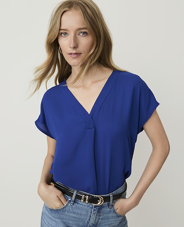 A woman in a blue v-neck top and jeans stands against a plain white background.