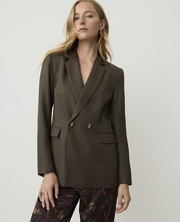 A woman in a dark brown double-breasted blazer and patterned pants stands against a plain white background.