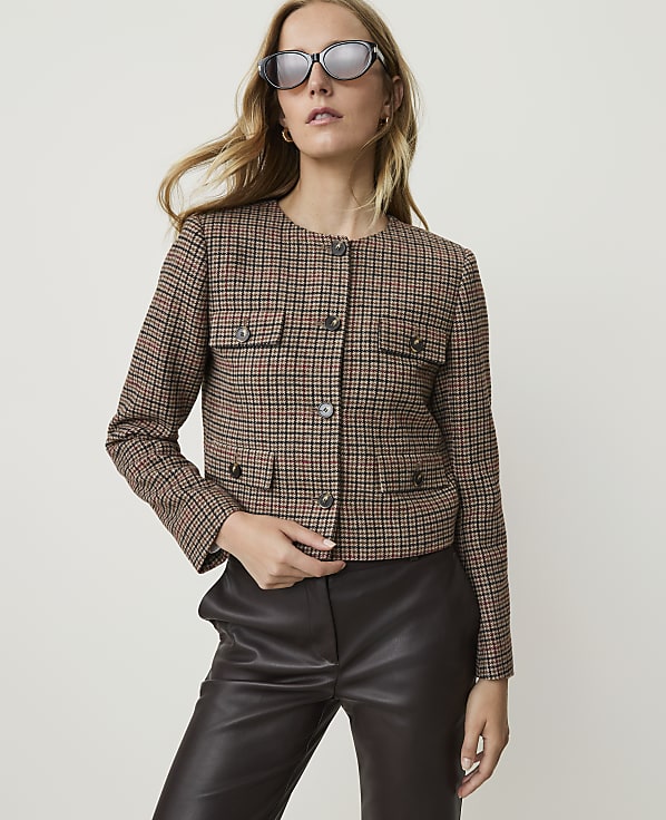 A woman in a plaid jacket and leather pants poses against a plain background.