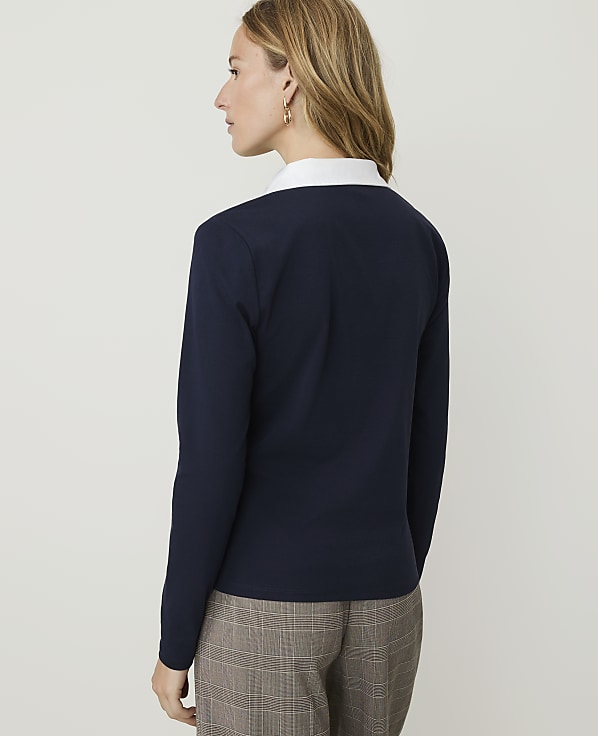A woman in a navy sweater and plaid pants stands against a plain white background.