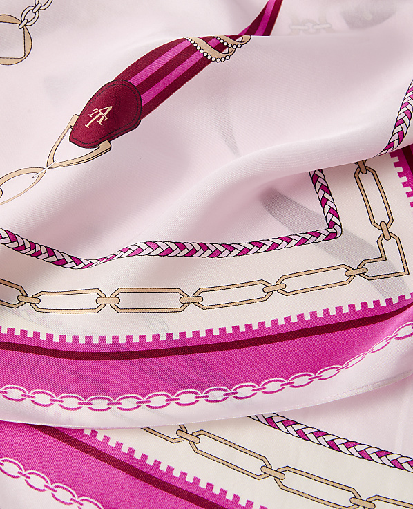 A pink silk scarf with a chain and equestrian-themed border is draped in soft folds.