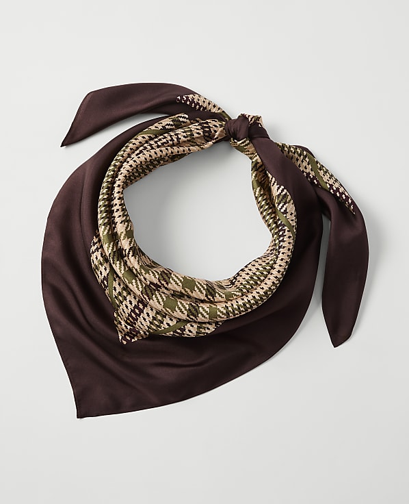 A brown silk scarf with a houndstooth pattern in green and beige is tied in a knot against a plain white background.