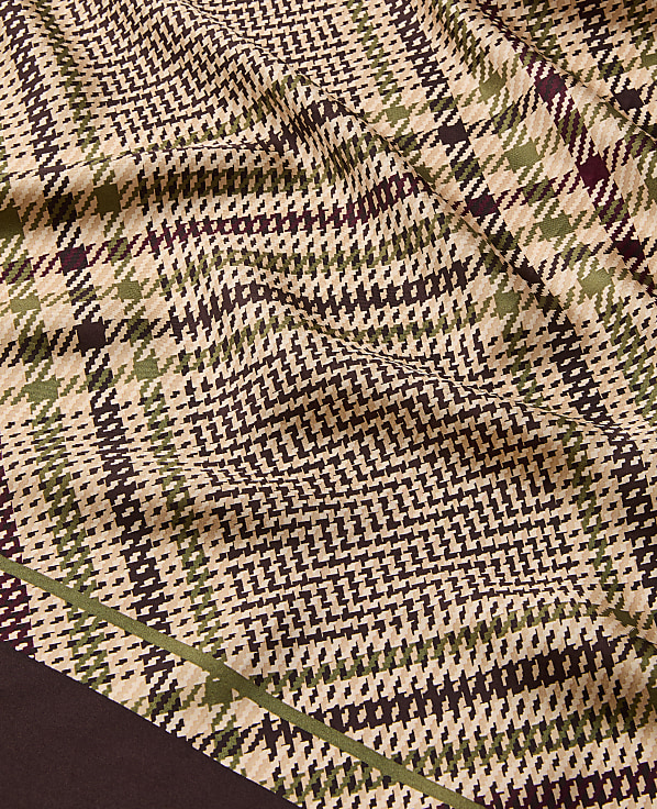 A close-up of a wrinkled fabric with a brown, green, and beige plaid pattern fills the foreground, while a dark brown border is visible at the bottom left.