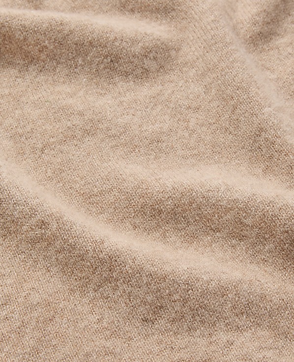 A close-up view of soft, beige fabric with gentle folds fills the frame, creating a textured and warm background.