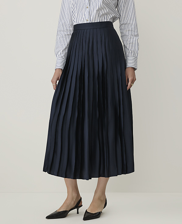 A person in a striped shirt and navy pleated skirt stands against a plain, light background.