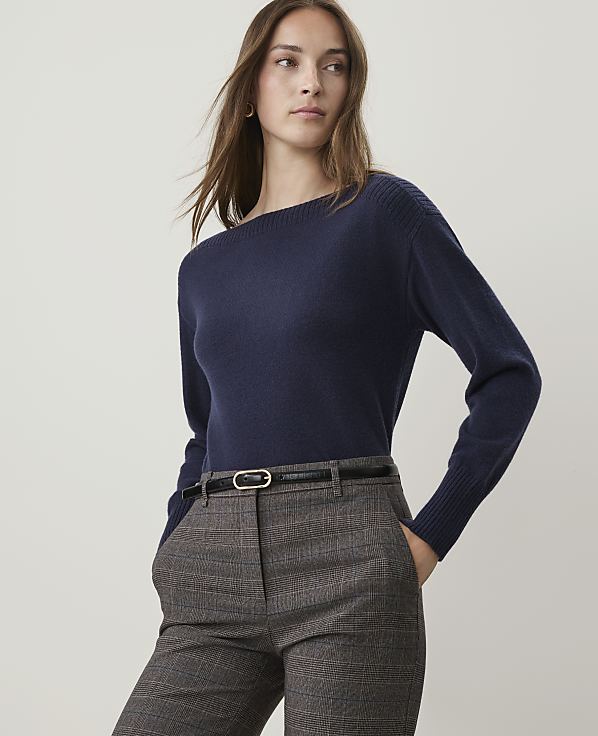 A woman in a navy sweater and plaid pants stands against a plain background.