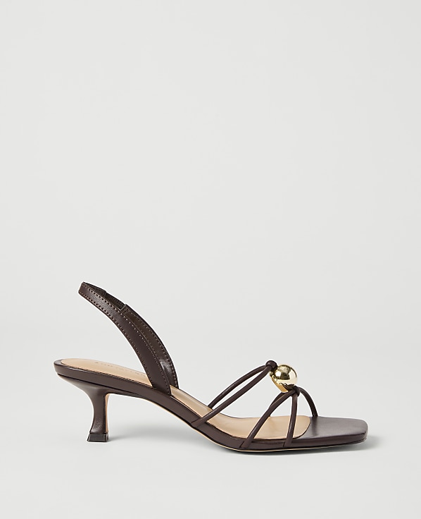 A brown strappy sandal with a gold bead detail rests on a plain white background.